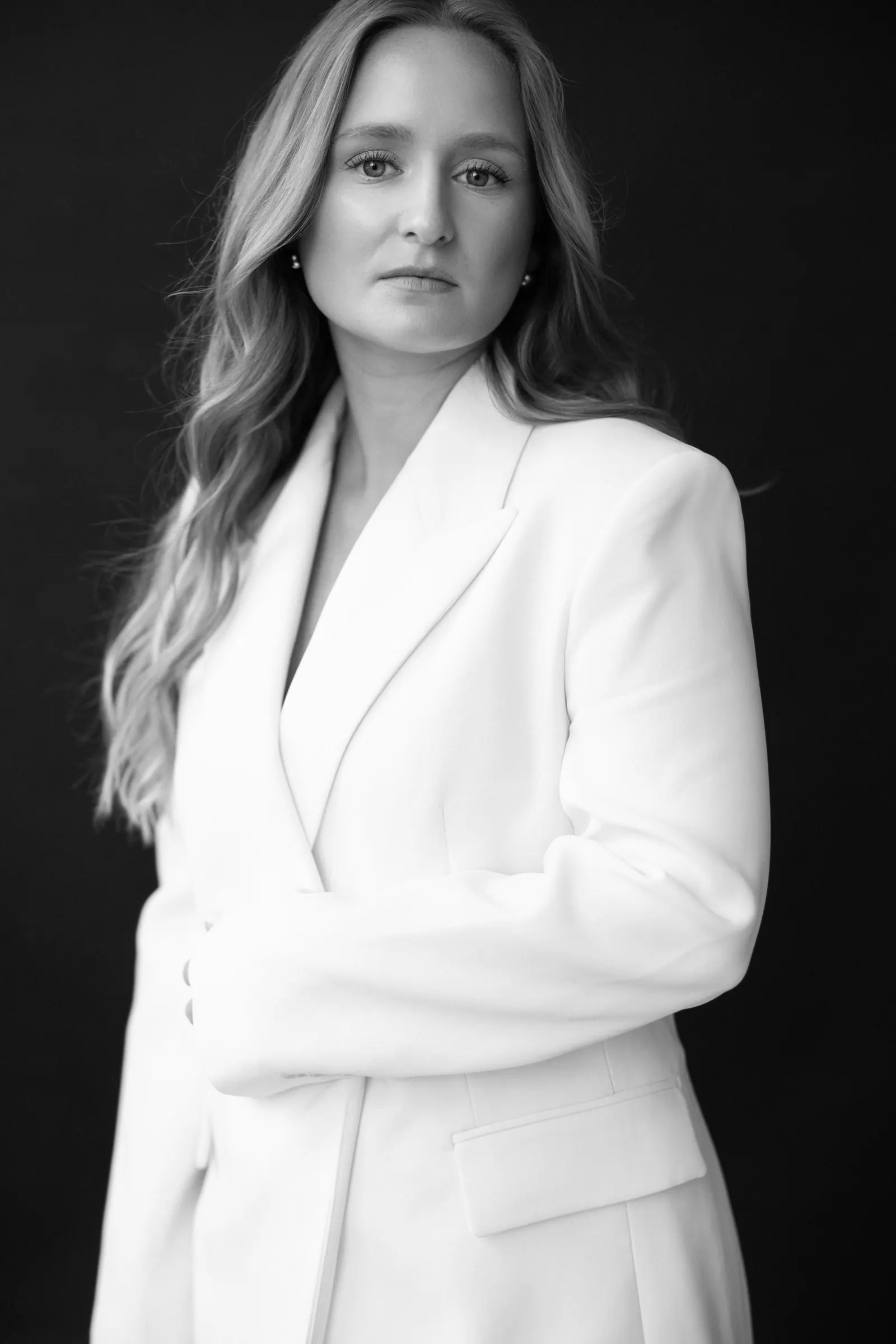 Black and white portrait of Aneta Studna, Prague wedding photographer, in a white blazer against a dark background