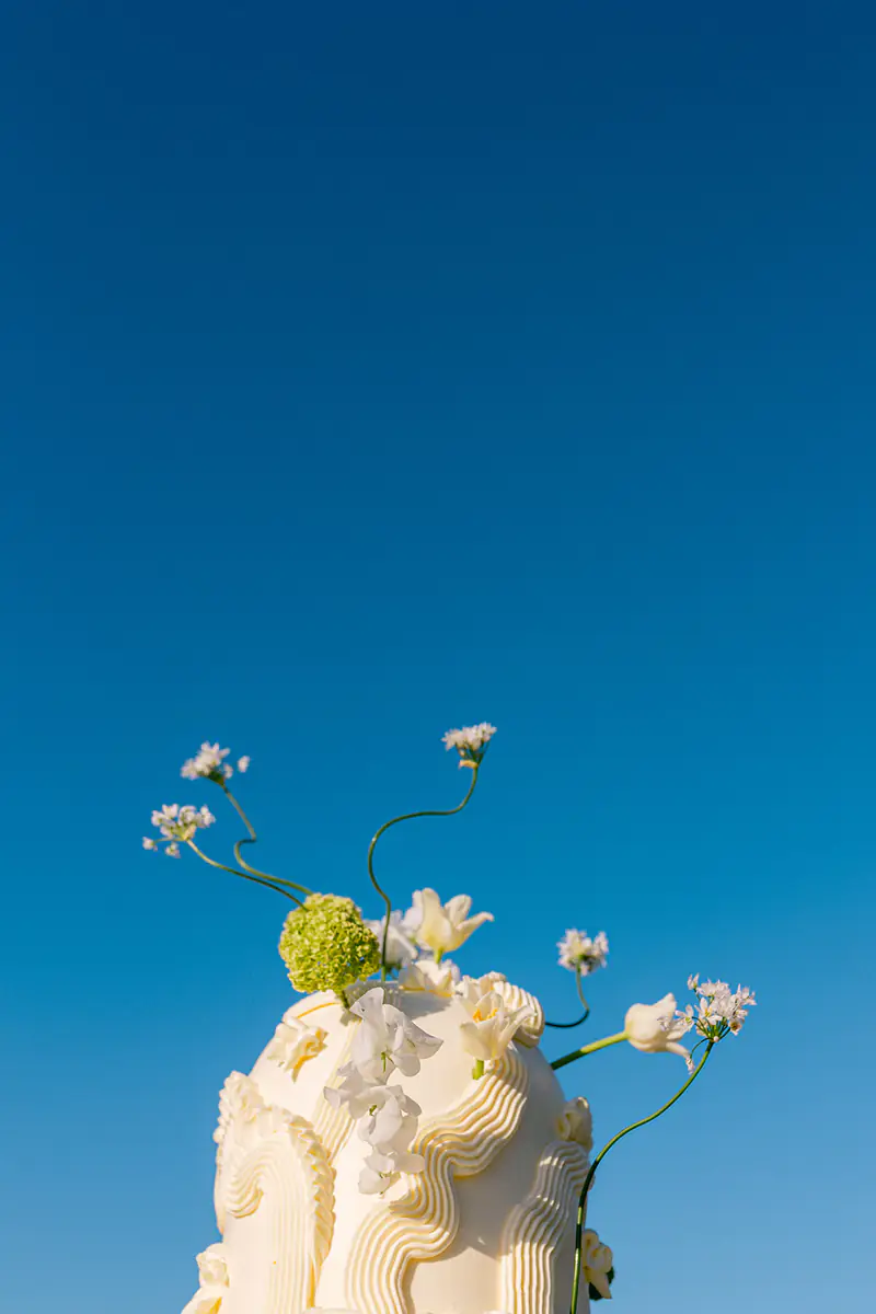 Sculptural white wedding cake topped with green flowers against a deep blue sky