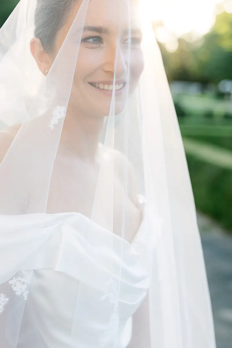 Smiling bride under a sheer veil in soft summer light