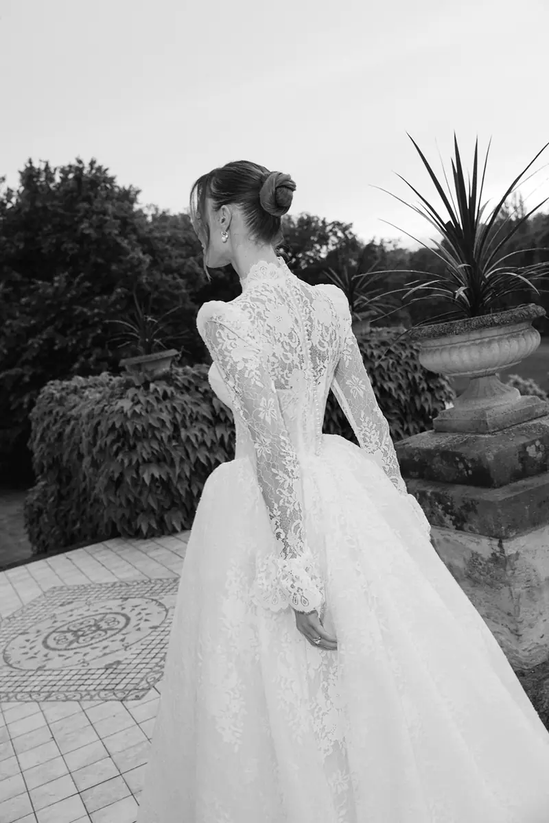 Black and white photo of the lace back of a bride’s long-sleeved wedding dress in a garden