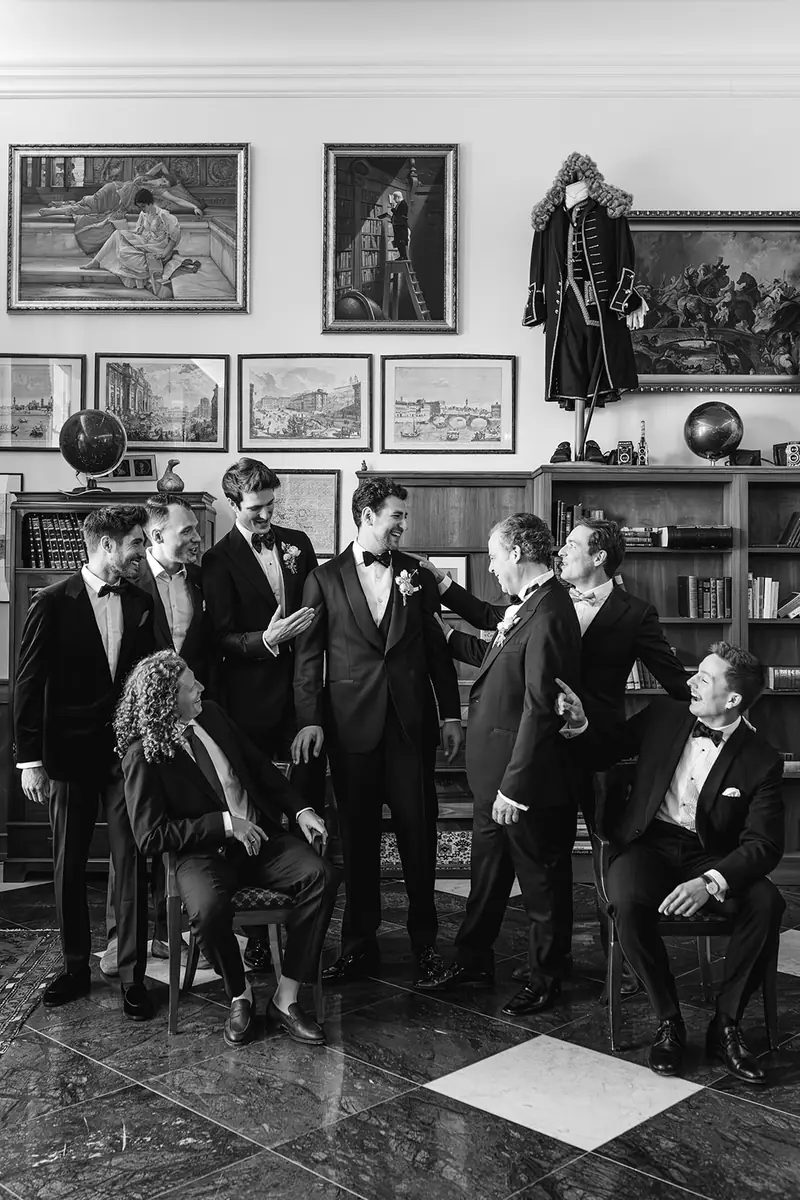 Black and white editorial group photo of the groom and groomsmen in tuxedos in a room hung with paintings