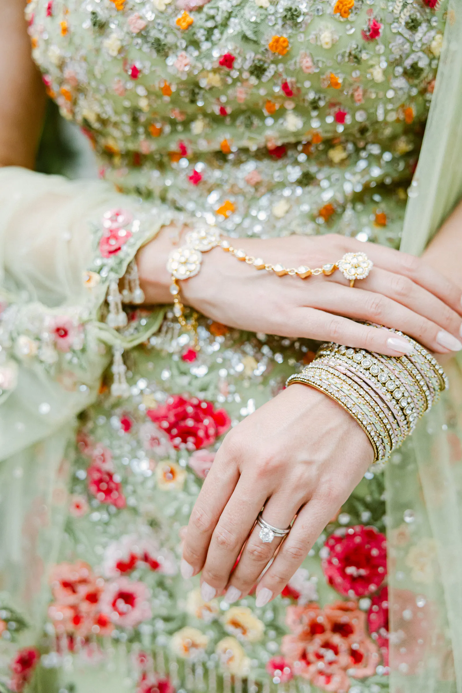 Close-up of a bride’s hands with gold bangles and rings against her colourful embroidered outfit at an Indian wedding