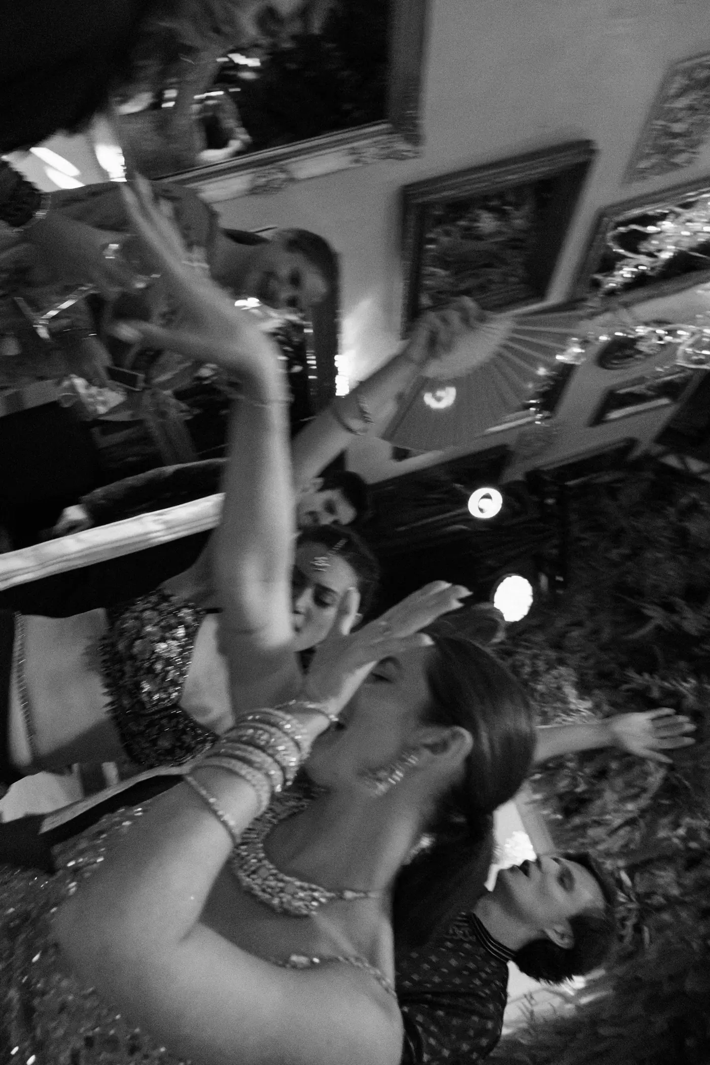 Black and white photo of guests dancing with raised arms under a mirrored ceiling