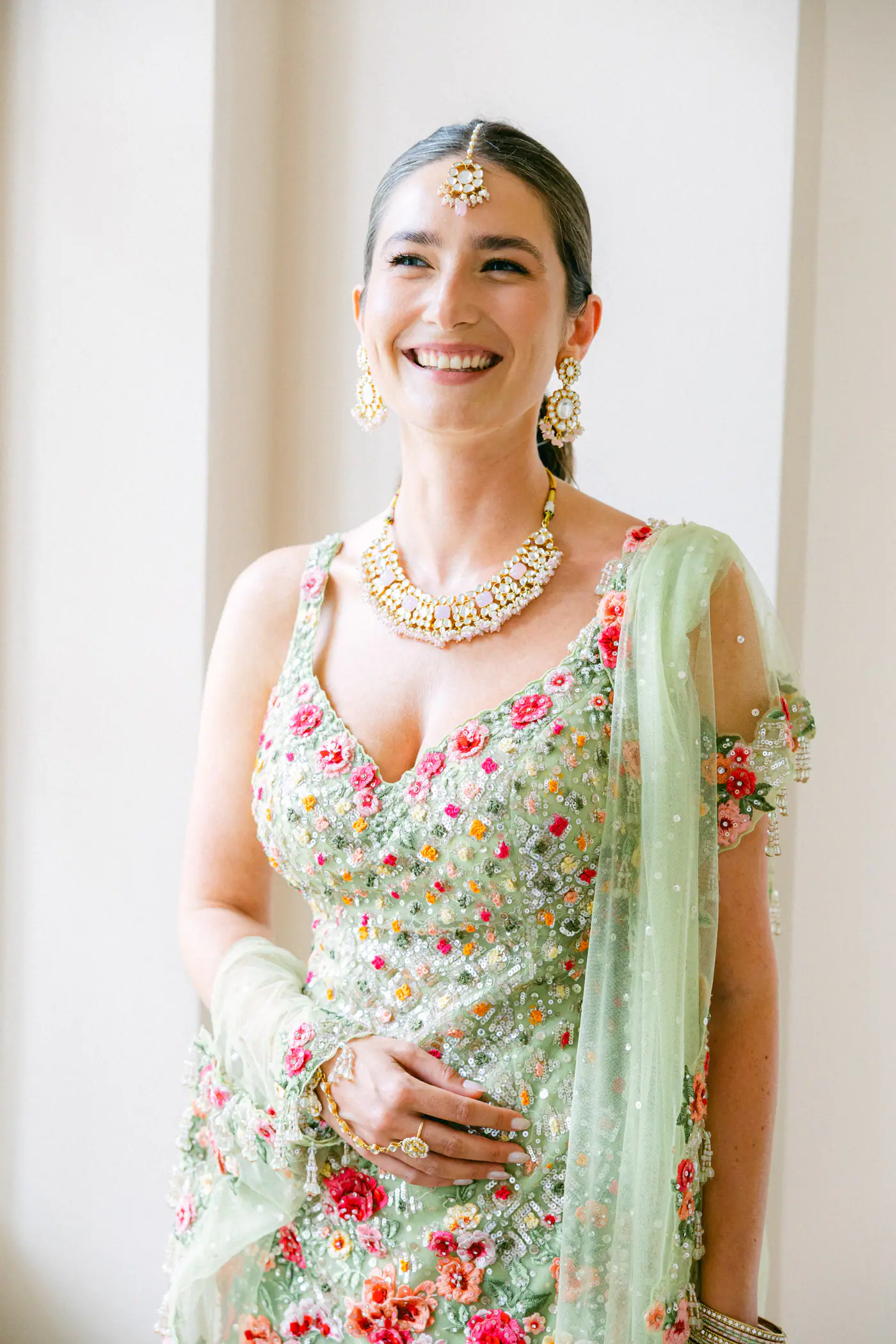 Smiling bride in a green embroidered lehenga by a window