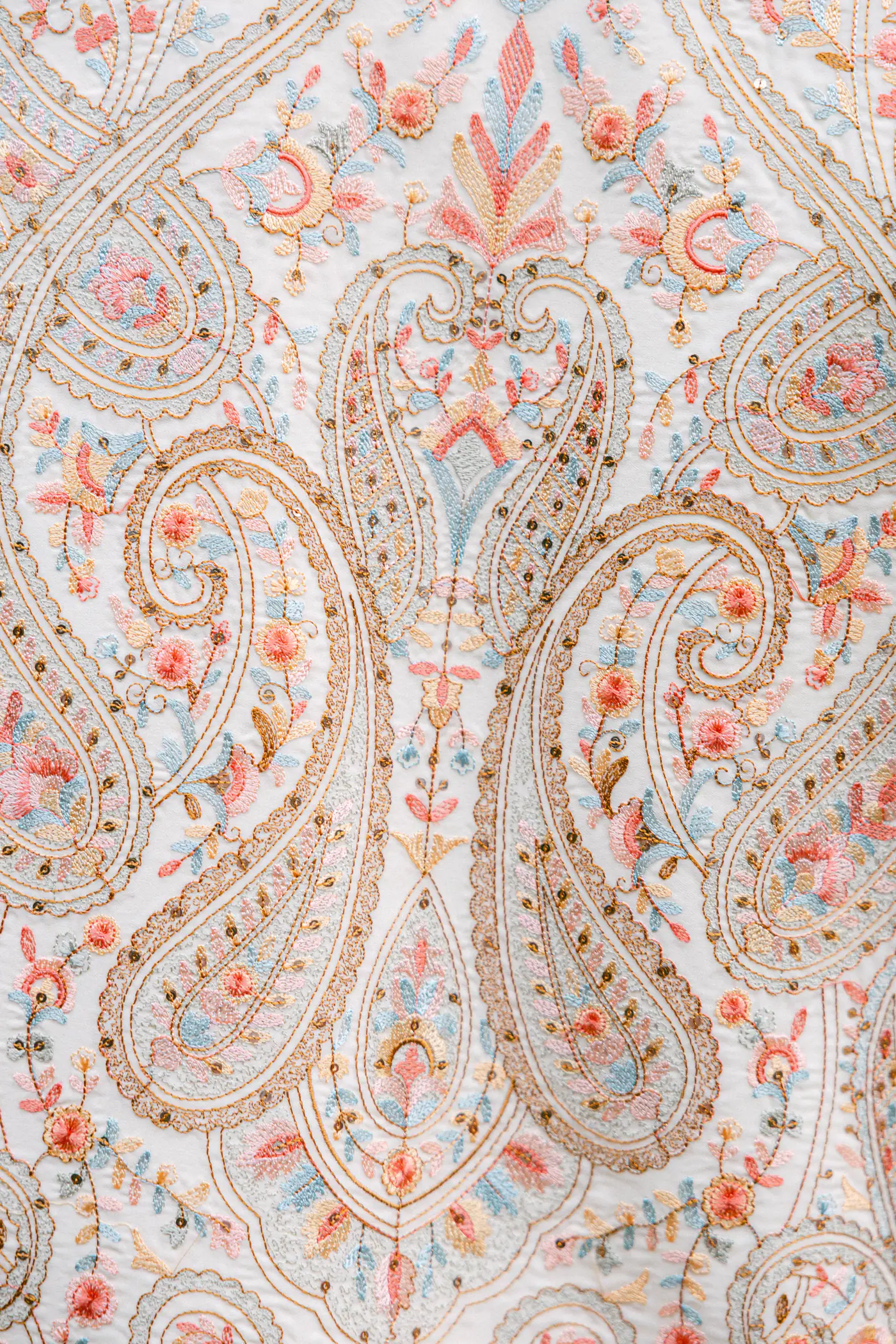 Close-up of pastel paisley embroidery on ivory fabric