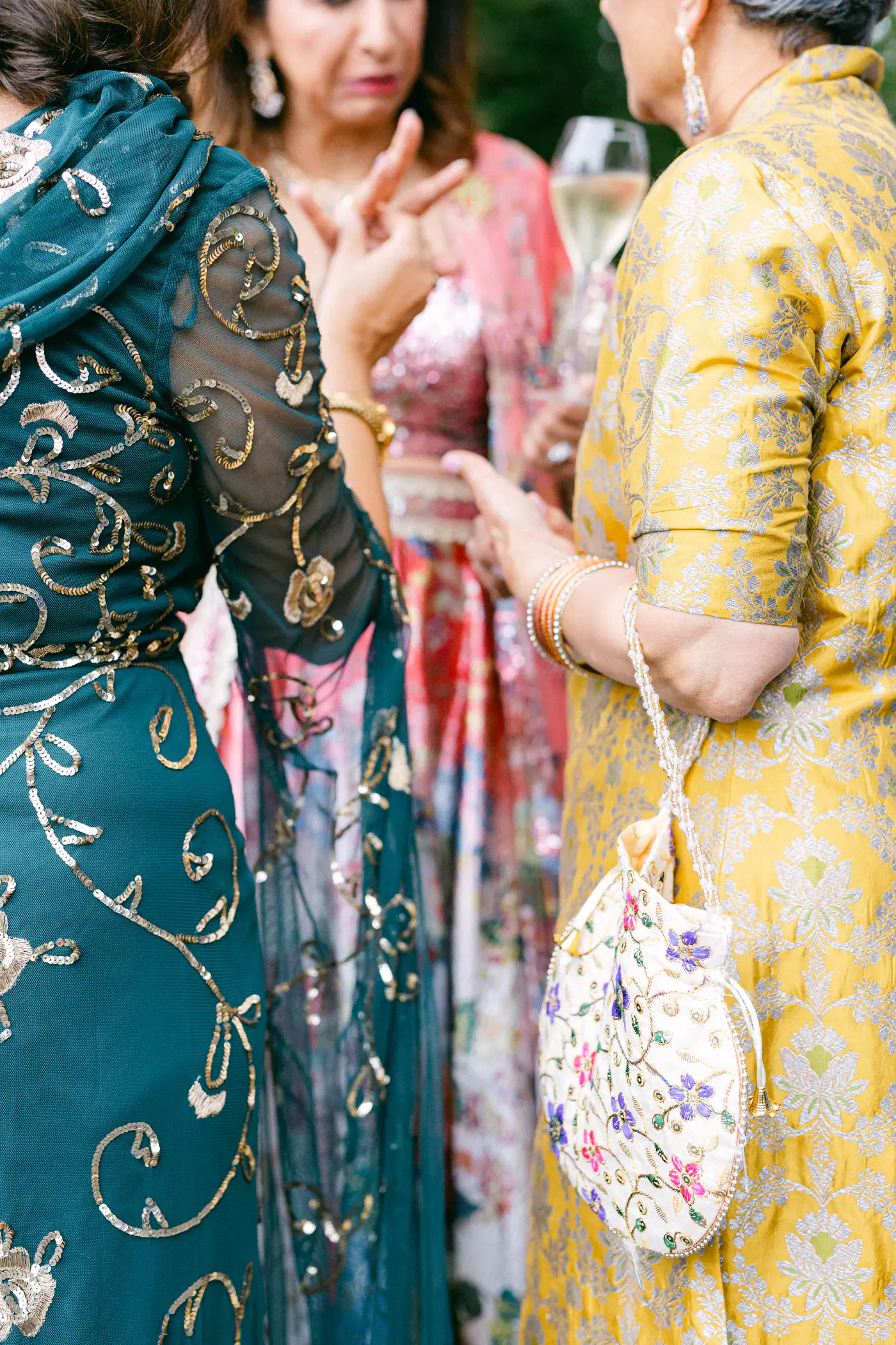 Guests in embroidered outfits talking, one holding a floral bag