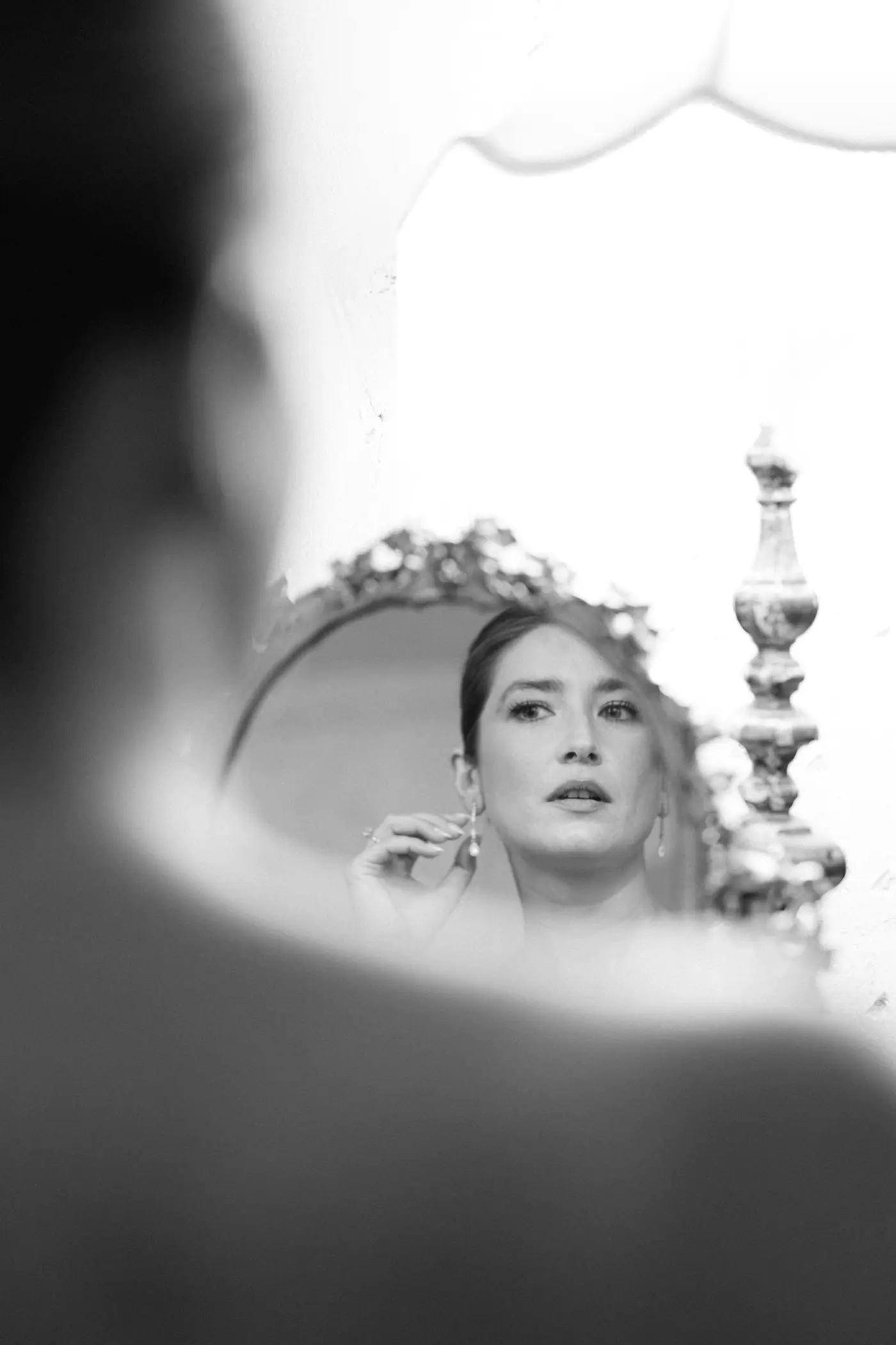 Black and white photo of the bride reflected in a mirror as she puts on her earrings
