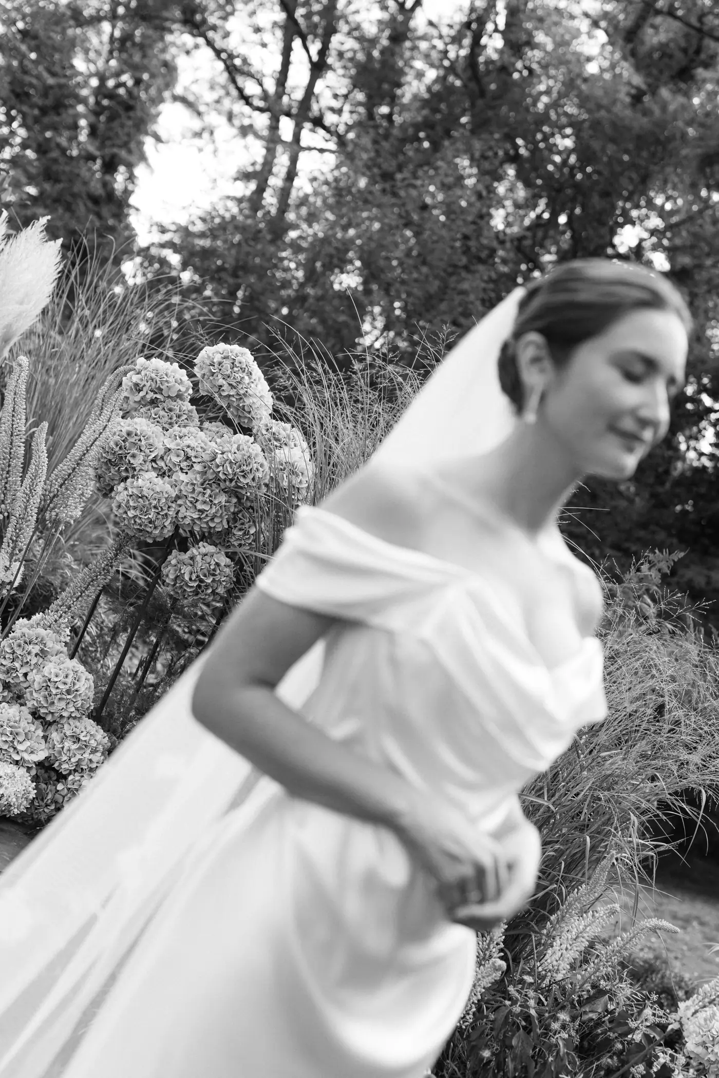 Black and white photo of the bride in an off-shoulder dress and veil among hydrangeas