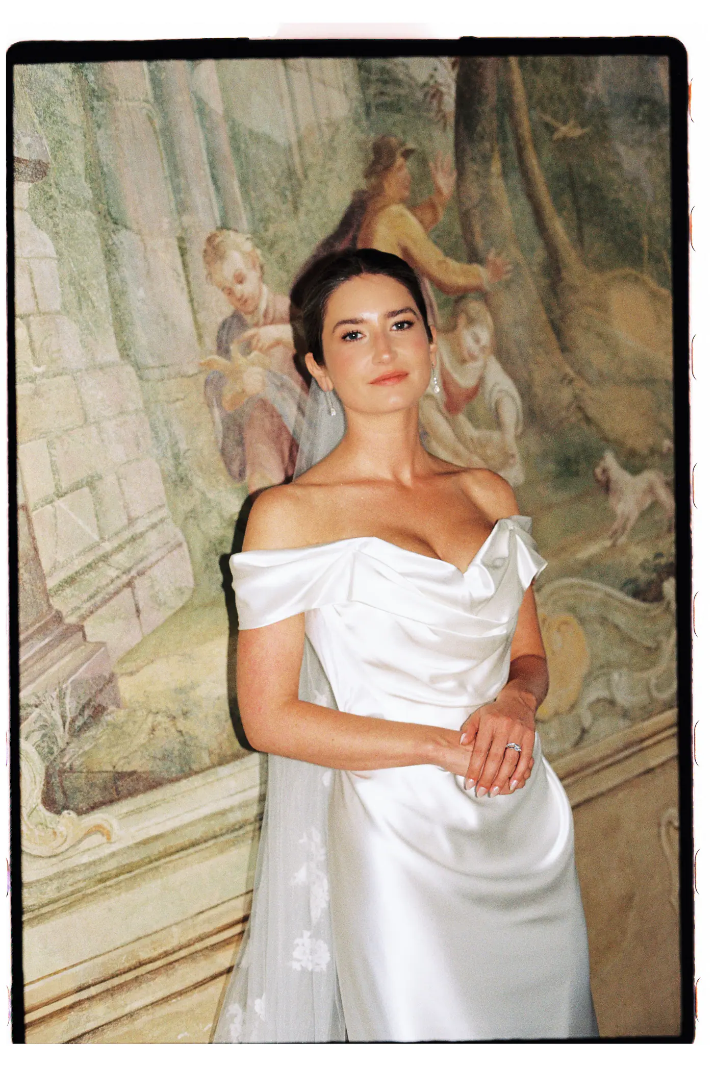 Bride in an off-shoulder satin dress in front of a painted fresco