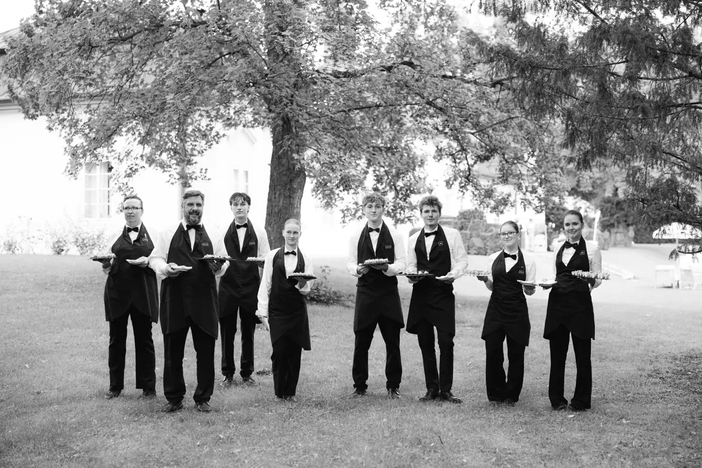 Black and white photo of the groom and groomsmen in tuxedos lined up under a tree