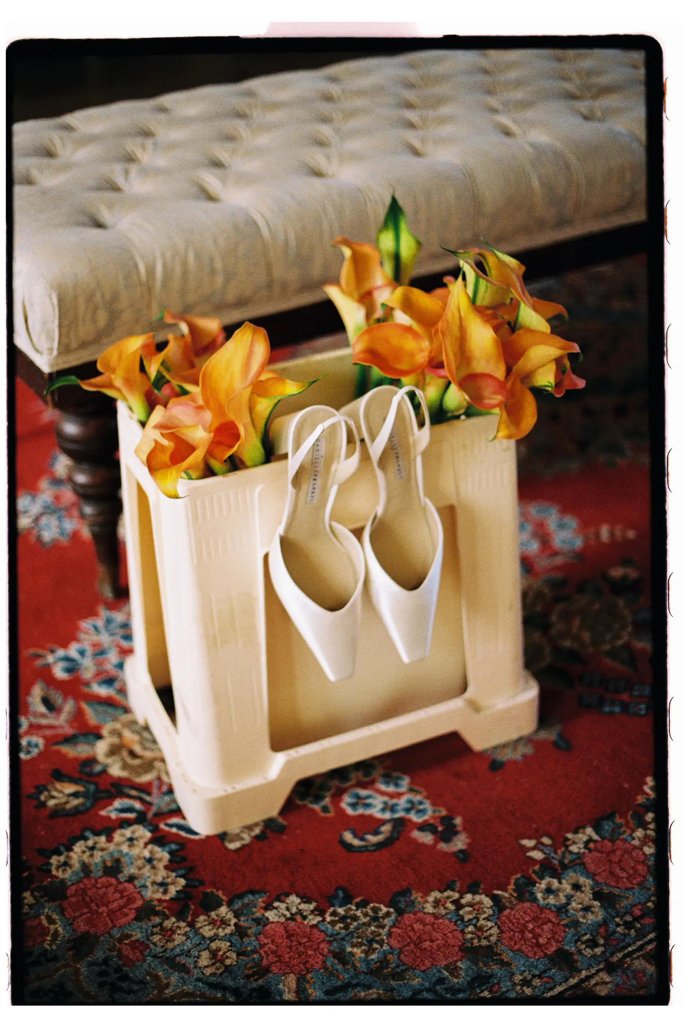 Bridal shoes on a footstool with orange lilies, on a red rug