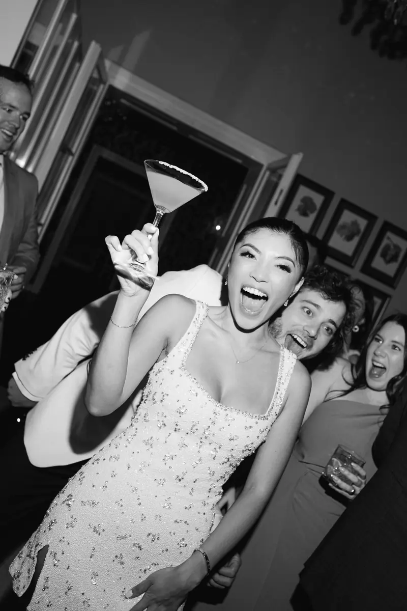 Black and white photo of a laughing bride raising a martini glass among her friends at Villa Richter in Prague