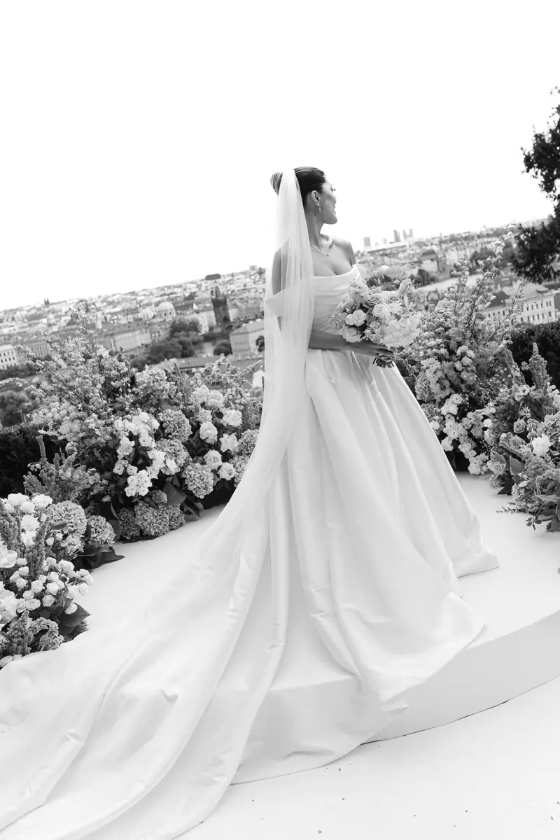 Black and white photo of a bride with a long train among hydrangeas above the Prague rooftops at Villa Richter