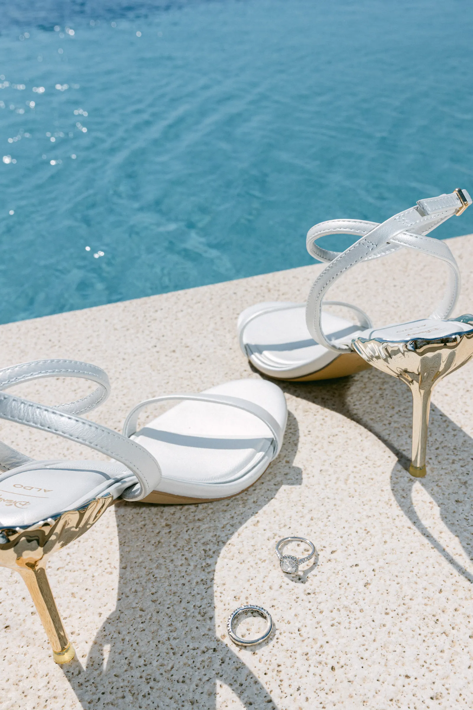 Bridal sandals with gold heels and wedding rings beside a turquoise pool