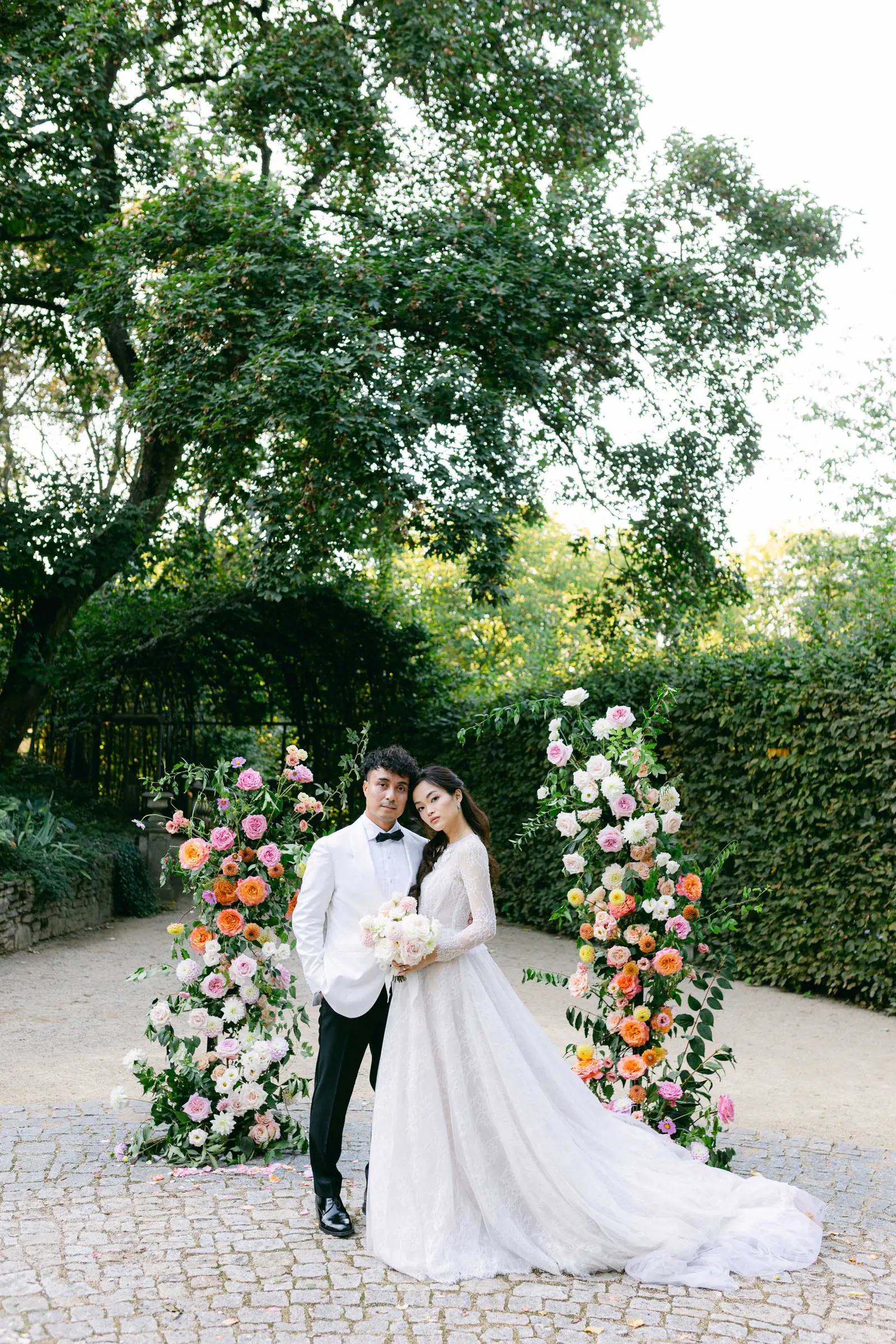 Bride and groom under a colourful floral arch in a garden courtyard