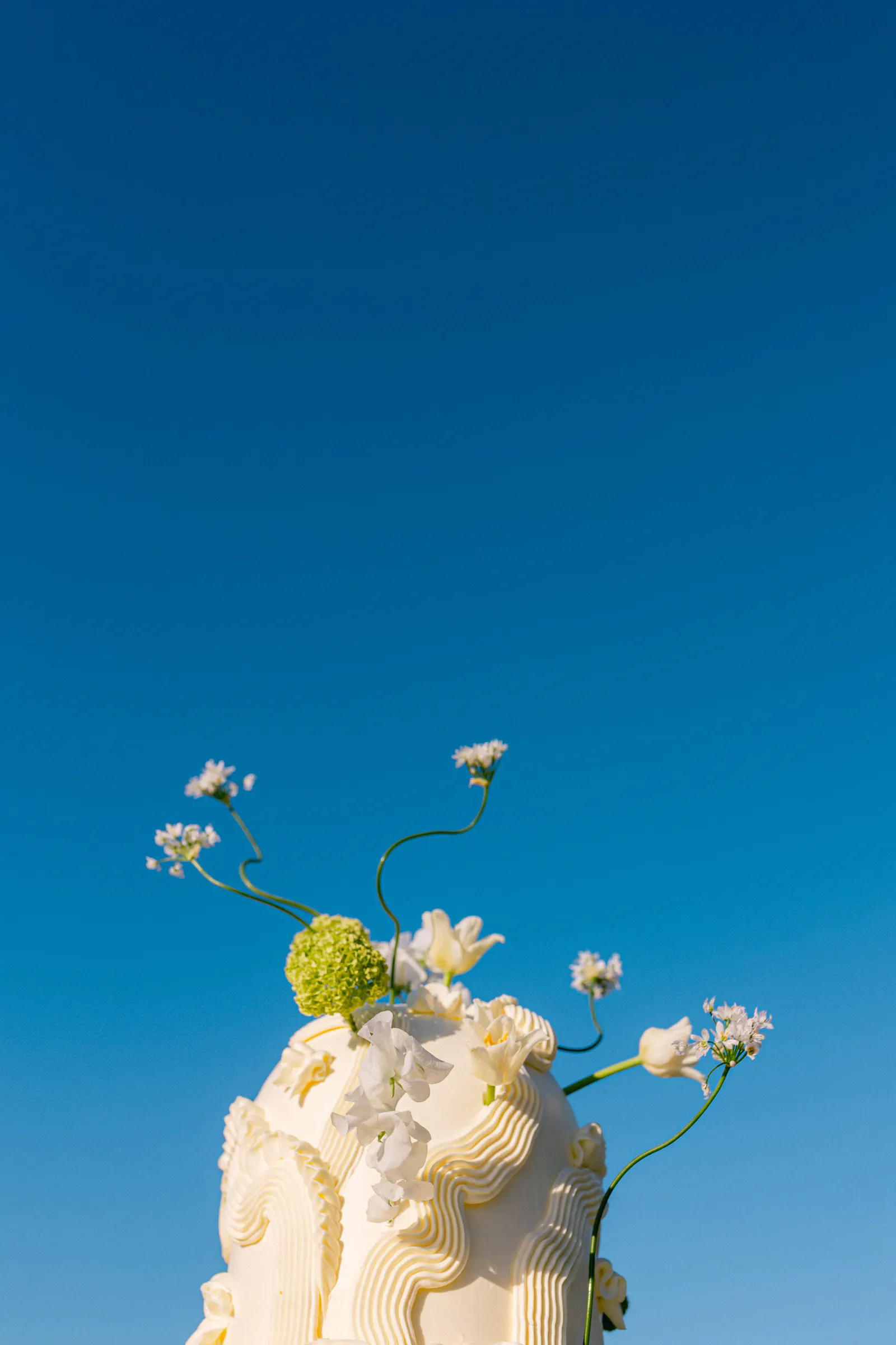 White floral wedding cake against a deep blue sky