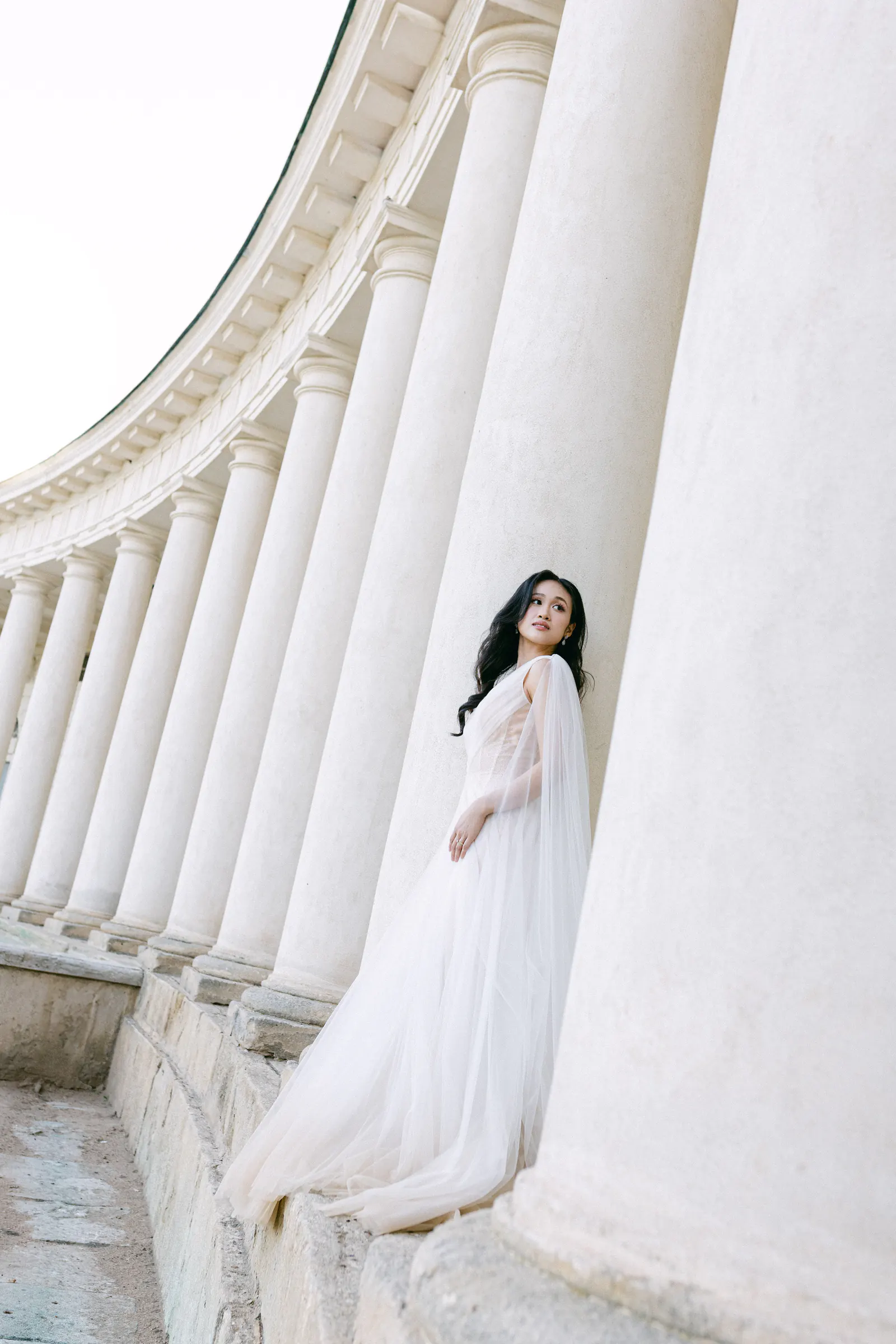Bride leaning against the white columns of a colonnade