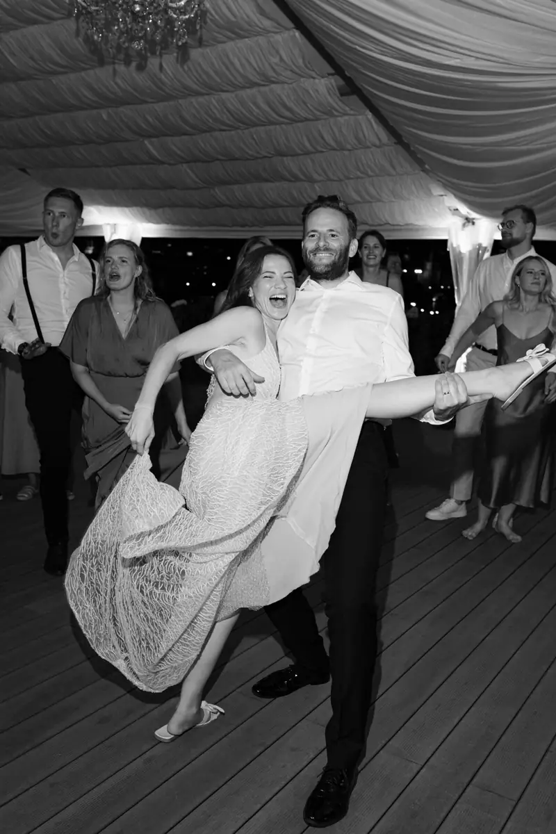 Black and white photo of a bride kicking her leg up while dancing with the groom at the wedding party