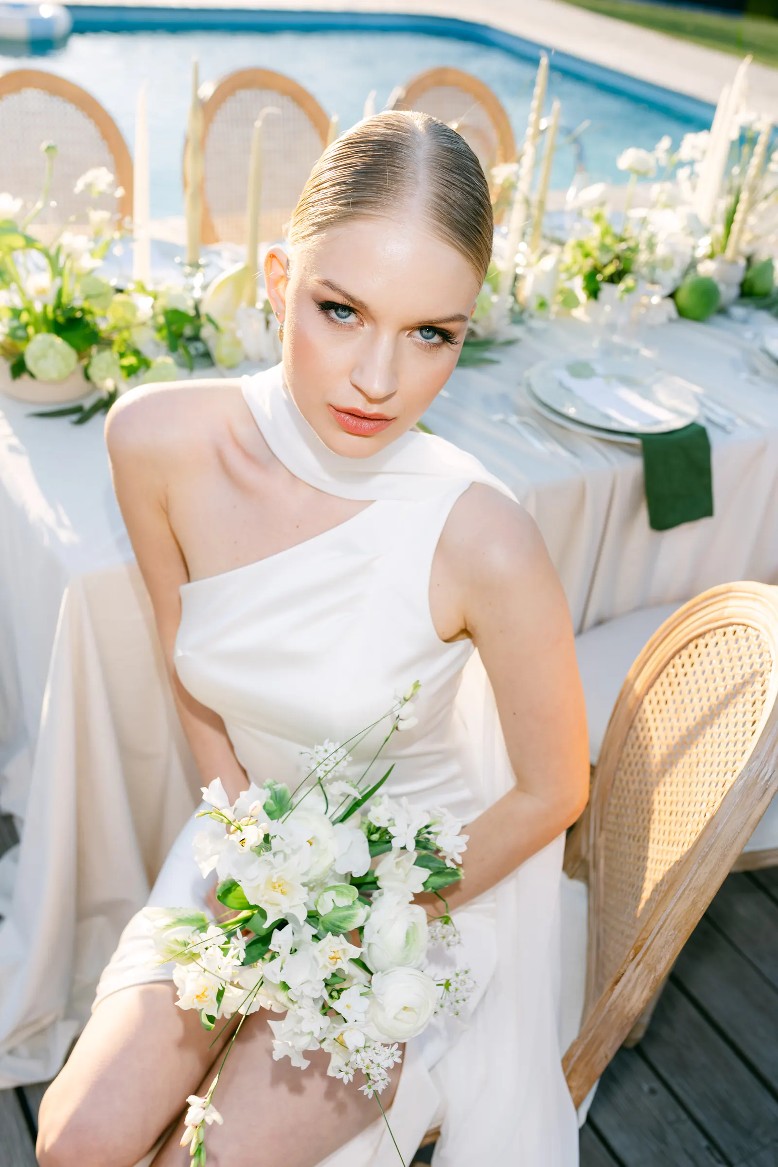 Bride in an off-the-shoulder gown with a bouquet beside a styled table