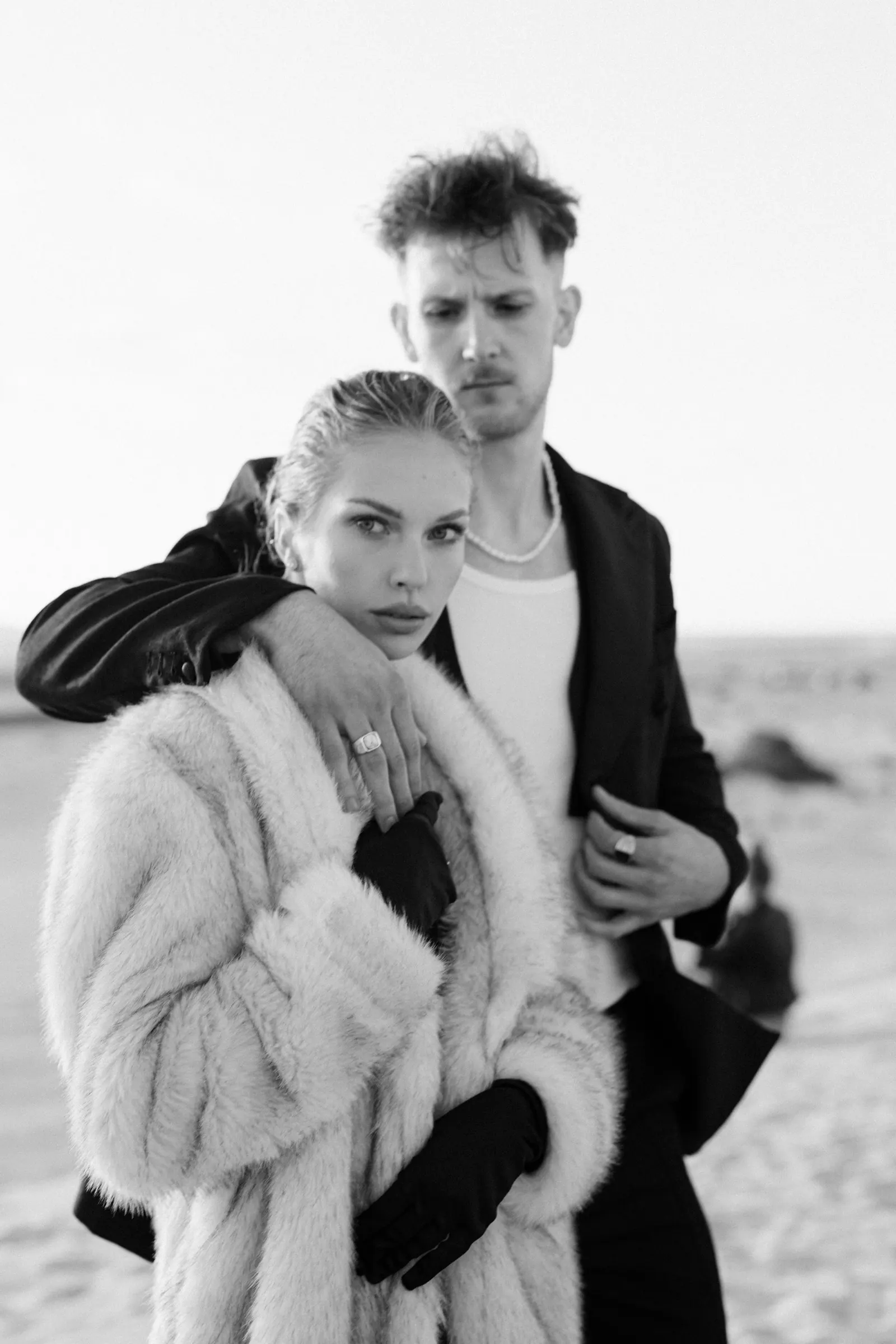 Black and white editorial portrait of a couple in a fur coat on the beach