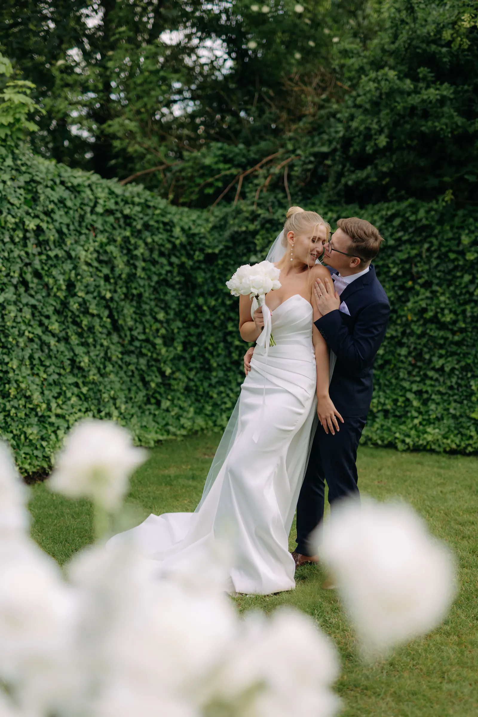 Couple kissing in a garden with white flowers in the foreground — Fara Brixi