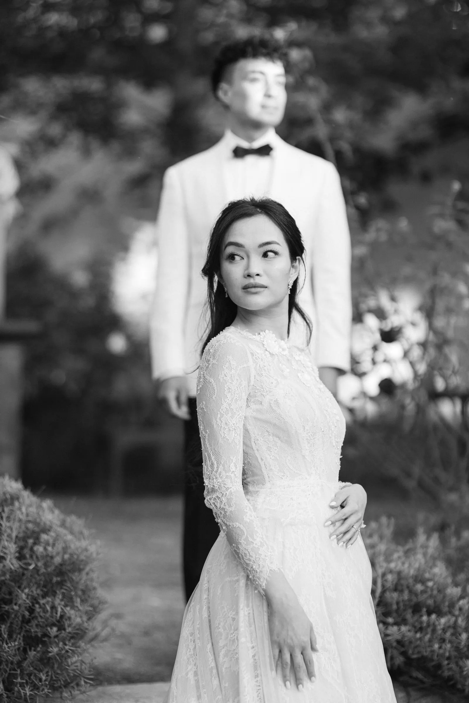 Black and white photo of the groom standing behind the bride in a lace dress